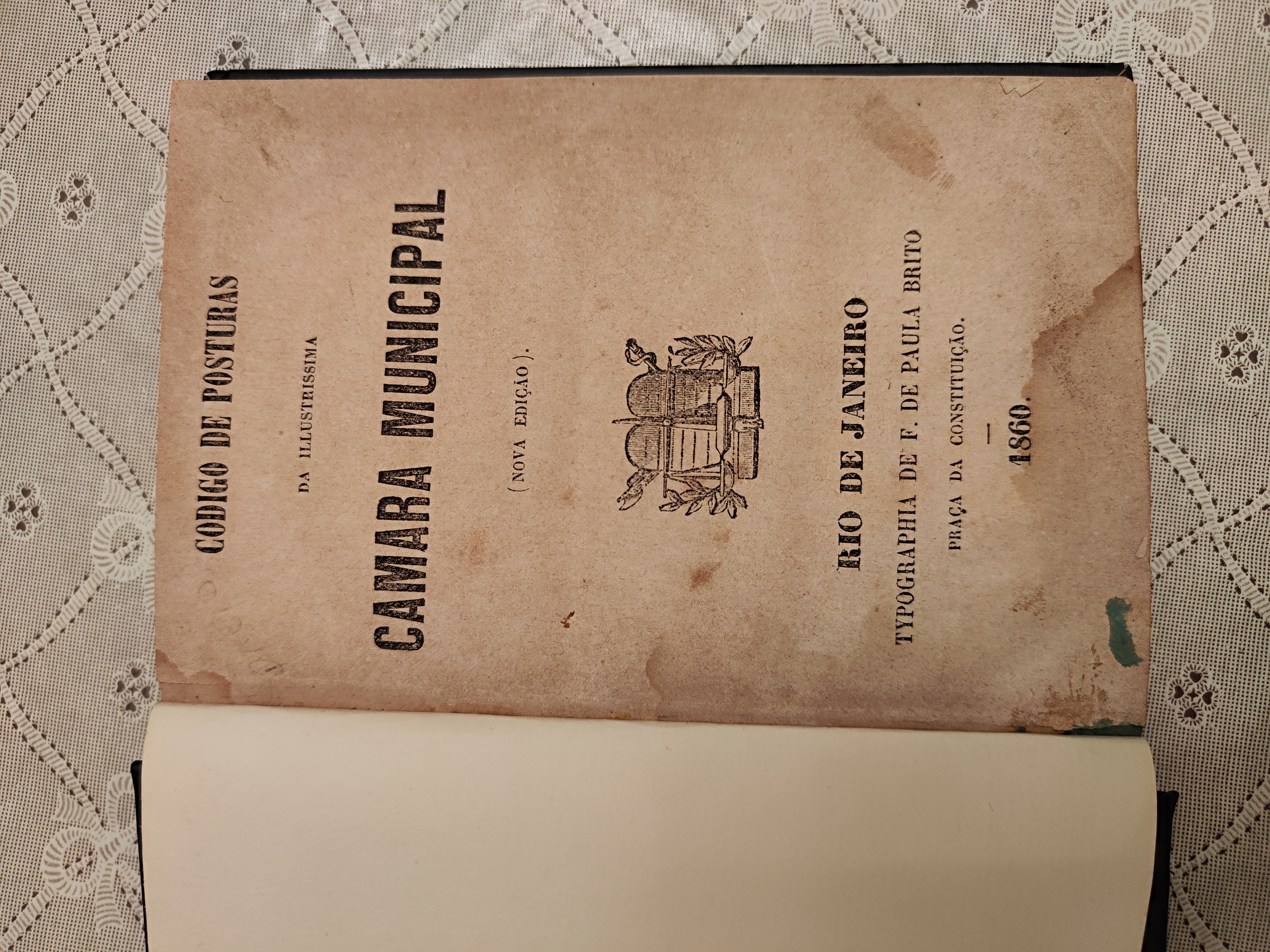 Contracapa do 'Código de Posturas' da Câmara Municipal do Rio de Janeiro, edição de 1860, impresso pela Tipografia de Francisco de Paula Brito. O livro tem páginas amareladas pelo tempo. Contém um brasão central com um feixe de ramos e um chapéu frígio, símbolo de liberdade. O título e as informações da edição estão dispostos em letras pretas, contrastando com o papel envelhecido. Francisco de Paula Brito (Rio de Janeiro, 2 de dezembro de 1809 – Rio de Janeiro, 5 de dezembro de 1861), mais conhecido como Paula Brito, foi um editor, jornalista, escritor, poeta, dramaturgo, tradutor e letrista negro e brasileiro. Atuou em diversas tipografias, tendo impresso o jornal O Mulato ou O Homem, título pioneiro da imprensa negra brasileira. Fundou a 'Sociedade Petalógica', da qual o jovem escritor Machado de Assis foi um membro destacado.